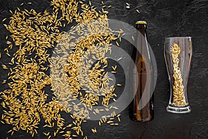 Grains of malting barley near beer bottle on black background top view