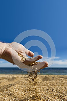 Grains of sand sifted through the fingers of male hands against the blue sea