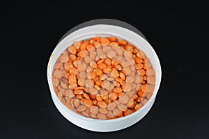 Grains, seeds of red lentils, a handful of lentils are located and scattered in a white plastic cover on a black plastic backgroun