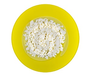 Grainy defatted cottage cheese in yellow plate isolated on white. Top view