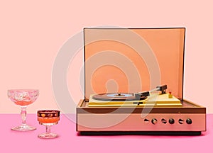 Gramophone record player from sixties. Turntable for single vinyl with pink bottom with light pink background. Two cocktail