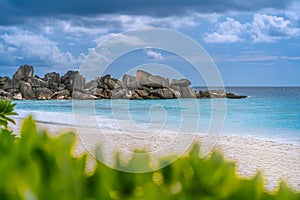 Grand Anse beach at La Digue island in Seychelles. White sandy beach with blue ocean lagoon. Green defocused foliage