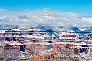 Grand Canyon in winter. Snow on red rocks; clouds on rim, blue sky overhead.