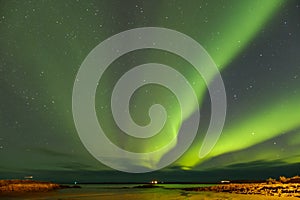 Grand green northern lights, sky full of stars, the lake can be seen in the foreground with a reflectio photo