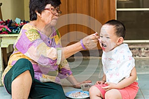 Grand mother feeding food to Thai baby boy