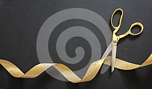 Grand opening. Gold scissors cutting gold satin ribbon, black background