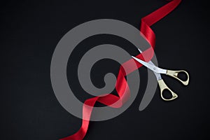Grand opening. Top view of gold scissors cutting red ribbon on black background.