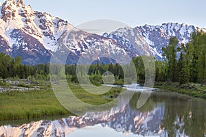 Grand Teton mountains above grassy valley and Snake River in early morning light