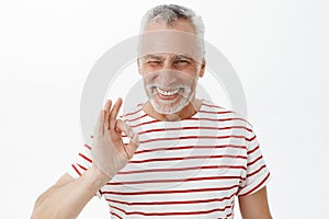 Grandad assuring he not tell parents. Portrait of kind and happy charismatic grandfather in striped t-shirt with white