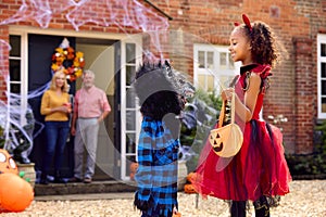 Grandchildren Dressing Up And Visiting Grandparent's House Trick Or Treating On Halloween