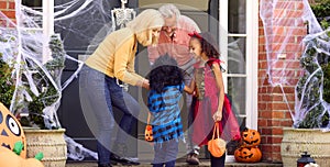 Grandchildren Dressing Up And Visiting Grandparent's House Trick Or Treating On Halloween