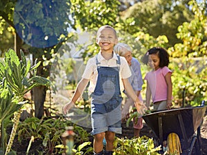 Grandchildren Helping Grandmother Working In Vegetable Garden Or Allotment With Barrow At Home