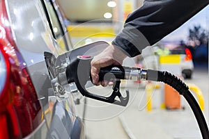 Granddad`s hand in black jacket refueling gray metallic car on gas station at night - close-up with selective focus