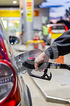 granddad& x27;s hand in black jacket refueling gray metallic car on gas station at night - close-up with selective focus