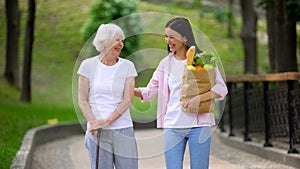 Granddaughter bringing food to elderly female patient, walking in hospital park