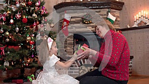 Granddaughter gives grandmother a Christmas present and kisses and hugs her by the tree