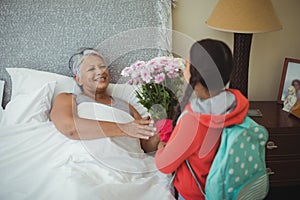 Granddaughter giving flowers to grandmother in bed room