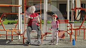 Granddaughter and grandfather doing fitness exercises with dumbbells. Senior man with child kid girl