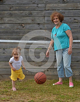 Granddaughter and grandmother play basketball on lawn in summer