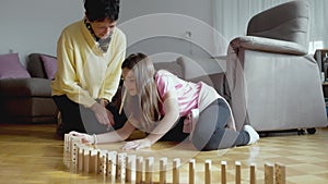 Granddaughter and grandmother playing with dominos on living room floor, young girl knocking down the dominos
