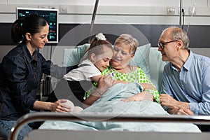 Granddaughter hugging sick elderly grandmother visiting her in hospital ward