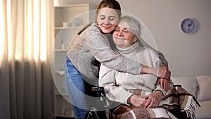 Granddaughter hugging smiling old woman in wheelchair, family love and care