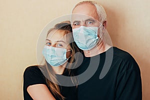 Granddaughter in a protective mask hugs her grandfather and cheers him up at a difficult time of limitations due to a sudden outbr
