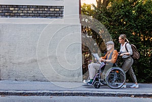 Granddaughter pushing senior man in wheelchair on street. Buying newspaper in newsstand. Female caregiver and elderly photo