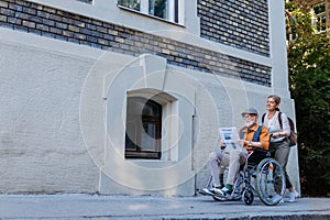 Granddaughter pushing senior man in wheelchair on street. Buying newspaper in newsstand. Female caregiver and elderly photo