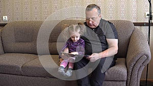 Granddaughter is reading a book with grandfather. The girl frowns at the book and listens carefully to Grandfather