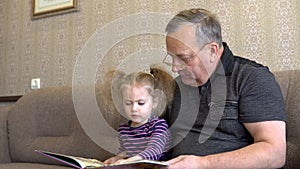 Granddaughter is reading a book with grandfather. The girl frowns at the book and listens carefully to Grandfather