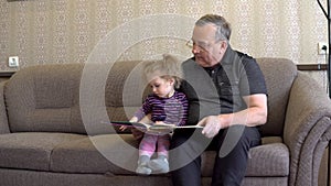 Granddaughter is reading a book with grandfather. The girl frowns at the book and listens carefully to grandfather