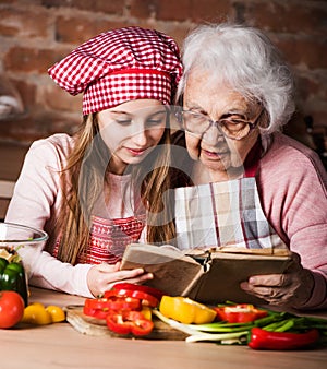 Granddaughter reading recipe book with granny