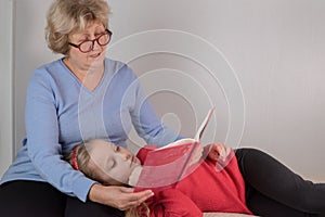 Granddaughter rest on grandmother`s lap and listen to a fairy tale.Loving grandmother reads a bok