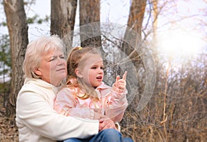 Granddaughter sitting in grandmother`s lap. Happy family.  Having good times with grandparent outdoors