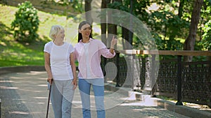 Granddaughter talking to aged woman walking with stick in park, old age health