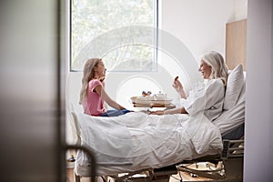 Granddaughter Visiting Grandmother In Hospital Bed For Afternoon Tea