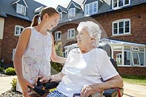 Granddaughter Visiting Grandmother Sitting In Motorized Wheelchair In Retirement Home photo