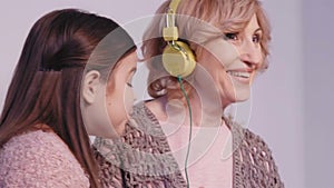 Granddaughter wears headphones to her grandmother. Woman gives five and together they begin to move rhythmically to