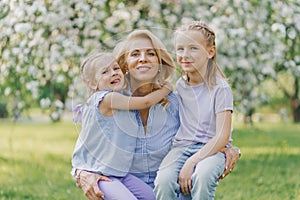 Granddaughters hug their grandmother in spring in a blooming garden outdoors