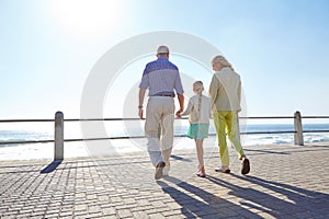 Granddaughters make every day special. grandparents walking hand in hand with their granddaughter on a promanade.