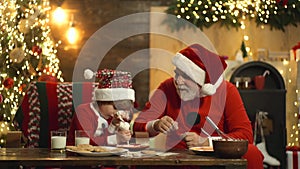 Grandfather baking christmas cookies with grangchild. Santa Claus bakes gingerbread for child in his kitchen before