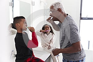 Grandfather In Bathroom Wearing Pajamas Brushing Teeth With Grandchildren photo