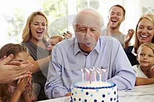 Grandfather Blows Out Birthday Cake Candles At Family Party