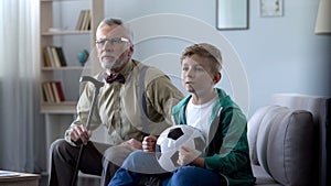 Grandfather and boy watching football at home, worrying about match result