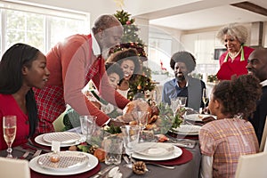 Grandfather bringing the roast turkey to the dinner table during a multi generation, mixed race family Christmas celebration, clos