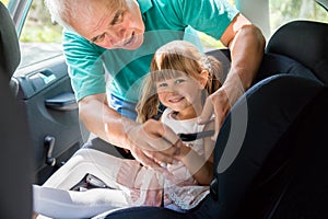 Grandfather Buckling Up On Granddaughter In Car Safety Seat