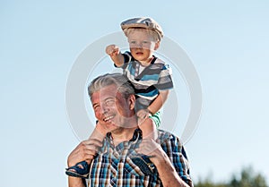 Grandfather carries grandson toddler boy on his shoulders