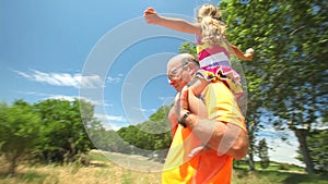 Grandfather carrying grand daughter on shoulders in nature in summer