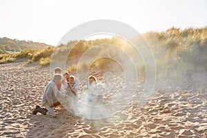 Grandfather Cooking As Multi-Generation Family Having Evening Barbecue Around Fire On Beach Vacation